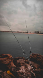 Fishing rod on rock by sea against sky