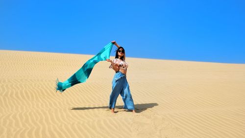 Full length of young woman holding scarf at desert on sunny day