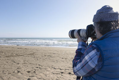 Rear view of man standing at beach against clear sky