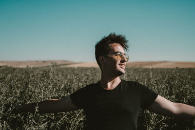 Young man standing on field against clear sky