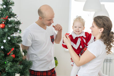 Mother and daughter standing against christmas tree at home