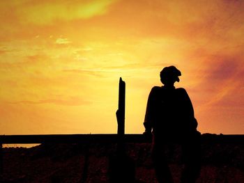 Silhouette person sitting on railing against sky during sunset