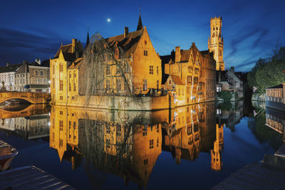 Reflection of illuminated buildings in canal against sky