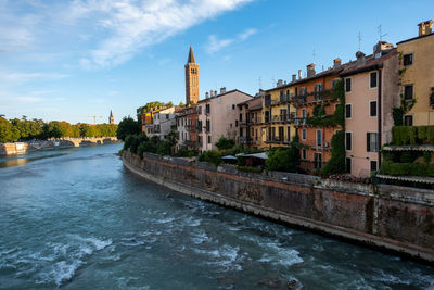 View of buildings by river against cloudy sky