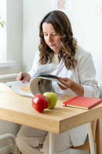 Portrait of smiling young woman using mobile phone while sitting on table