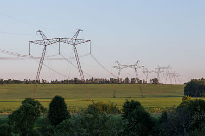 Scenic view of power line towers on green summer field against sky at evening  light