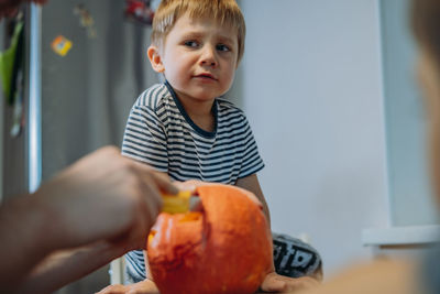 Caucasian man with his cute sons drawing out eyes on a pumpkin to make traditional jack lantern.