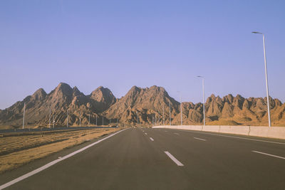 Road leading towards mountains against clear sky