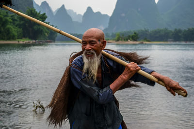 Smiling fisherman holding bamboo at river