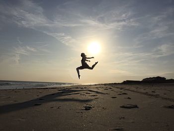 Woman jumping at beach against sky on sunny day