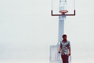 Man holding mobile phone and book while standing against wall at basketball court