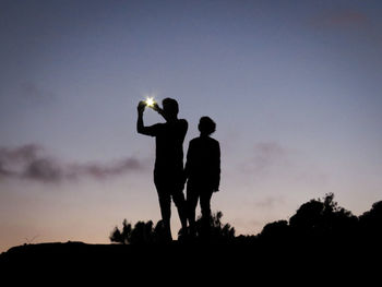 Silhouette man and woman standing against sky at night