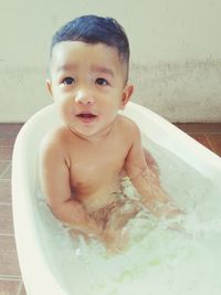 Portrait of cute baby boy sitting in bathtub at bathroom