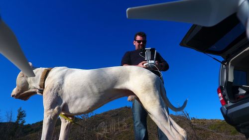 Man using drone remote control by dog while standing against clear blue sky