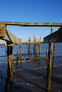 Wooden posts in sea against clear blue sky