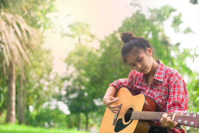 Young woman playing guitar against blurred background