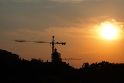 The silhouettes of two cranes in the city at sunset