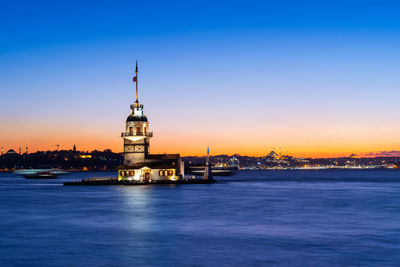 Illuminated buildings by sea against sky during sunset