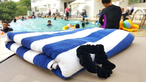 Close-up of towel and hair elastic against people in swimming pool