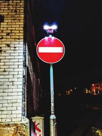 Illuminated road sign against building at night