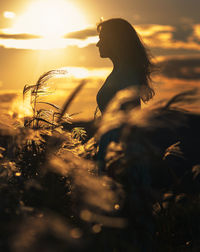 Woman standing by plants on field against sky during sunset