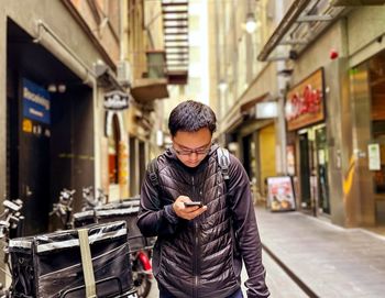 Portrait of young asian man using mobile phone in alley against buildings in the city.