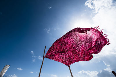 Low angle view of fabric tied on bamboos against blue sky during sunny day