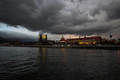 River by city against cloudy sky at dusk