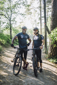 Smiling male friends with cycles standing on footpath