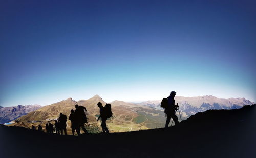 Silhouette hikers hiking on mountain against blue sky