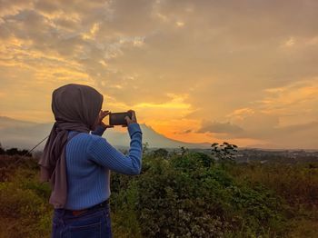 Rear view of senior woman photographing sky during sunset