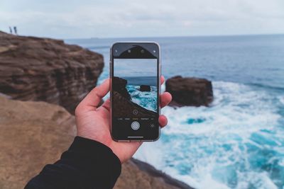 Midsection of man holding camera at beach against sky