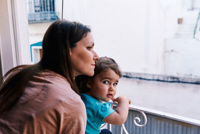 Mother and daughter looking out the window of the house happy