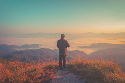 Rear view of man standing on land against sky during sunset