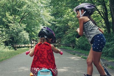 Rear view of girl on push scooter by sister cycling toy bicycle over footpath