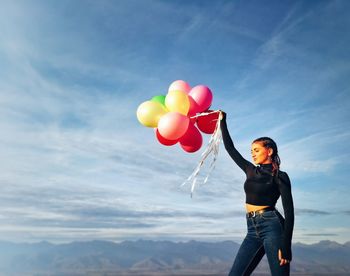 Full length of woman holding balloons against sky