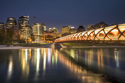 Illuminated bridge over river by buildings against sky at night