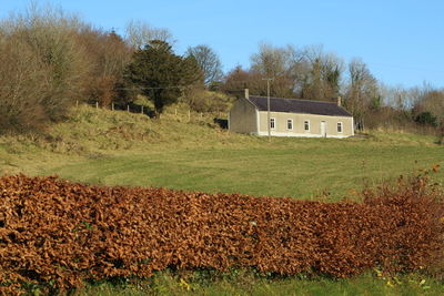 House on field by trees against sky