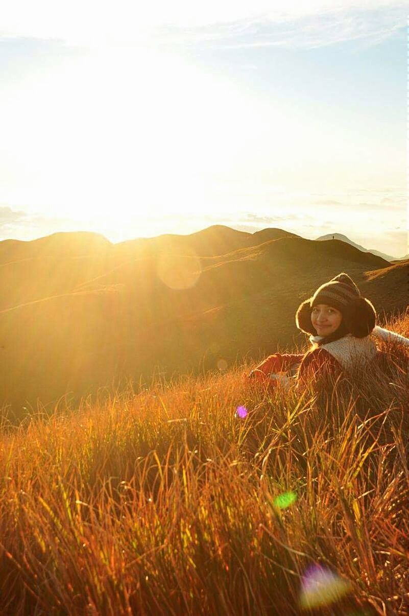 landscape, sky, field, tranquil scene, tranquility, grass, beauty in nature, sun, scenics, nature, sunlight, mountain, sunset, lens flare, one person, plant, sunbeam, non-urban scene, growth, rural scene