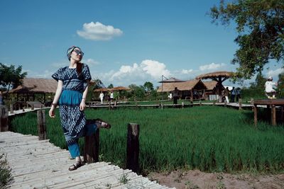 Woman standing on pier over field against sky