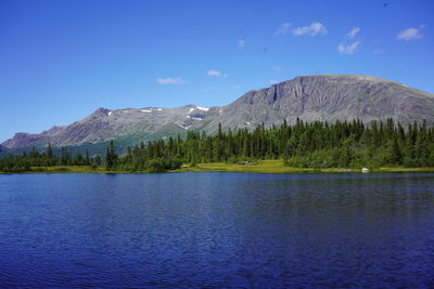 Scenic view of lake by mountains against blue sky