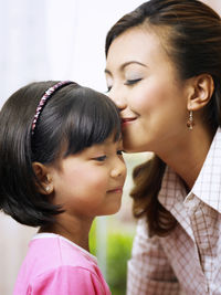Smiling mid adult woman kissing daughter forehead