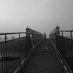 Man on footbridge against clear sky