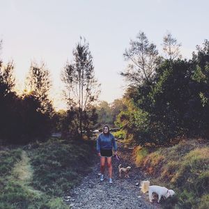 Rear view of women standing on footpath amidst trees against sky