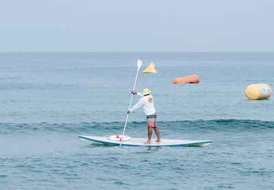 Man paddleboarding in sea against clear sky