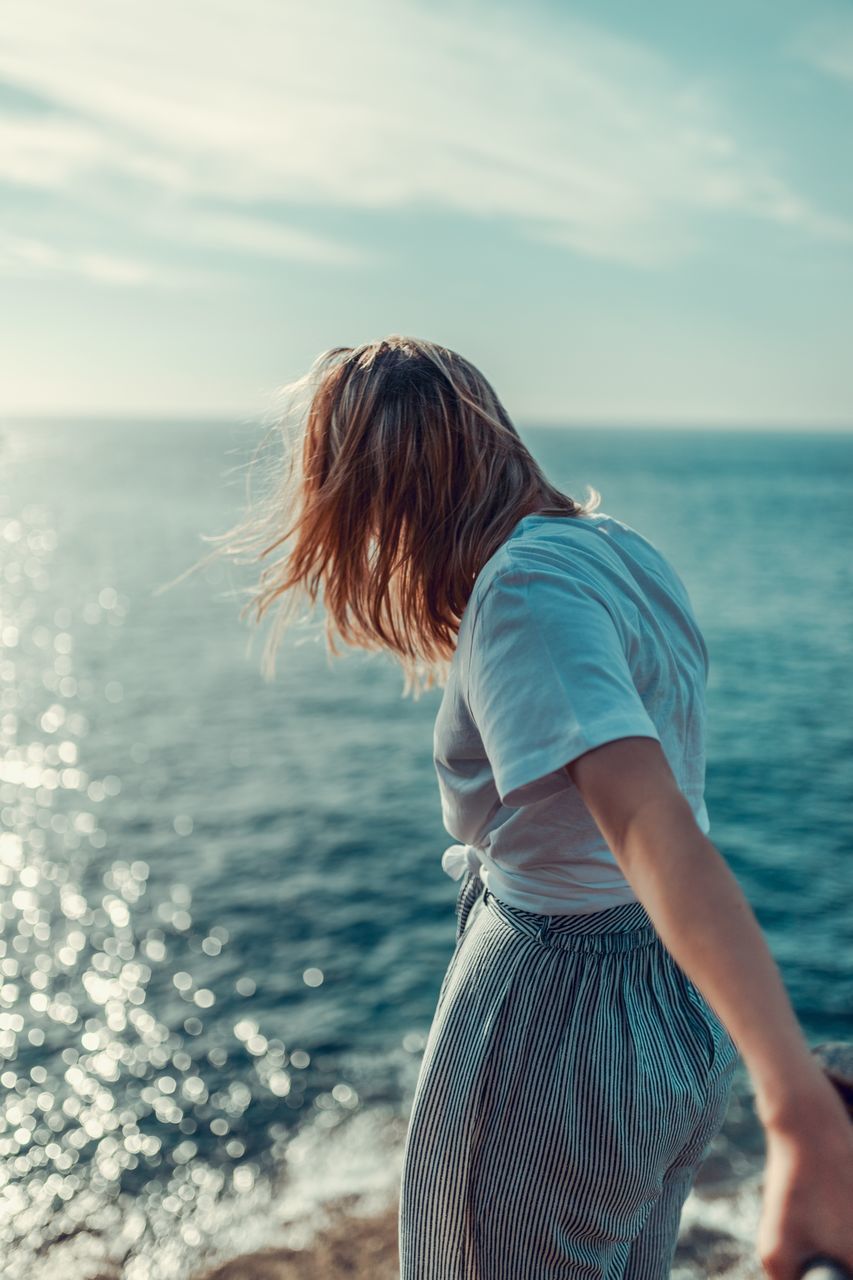 water, sea, one person, real people, leisure activity, sky, women, lifestyles, standing, casual clothing, hair, adult, three quarter length, beauty in nature, horizon, nature, hairstyle, scenics - nature, horizon over water, tousled hair, outdoors, hair toss