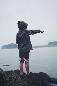 Rear view of a boy looking and pointing at sea against sky