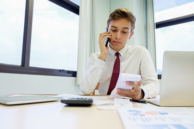 Businessman with bill talking on phone while working at desk in office