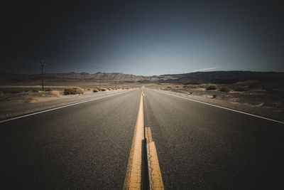 Diminishing perspective of empty road along landscape against clear sky