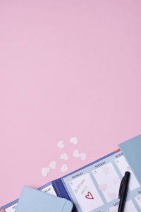 Heart-shaped confetti and calendar on pink background